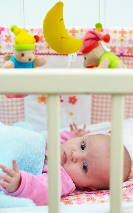 baby lying in a white crib with a crib mobile overhead